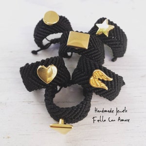 May include: Five black braided rings with gold charms. The charms include a circle, a square, a star, a heart, and a pair of wings. The rings are handmade and the text "Handmade Jewels Fatto Con Amore" is visible in the image.
