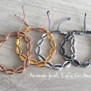Könnte beinhalten: Drei Armbänder aus kleinen Muscheln und verstellbaren Schnüren. Die Armbänder sind in Roségold, Gold und Silber gehalten. Der Text "Handmade Jewels Fatto Con Amore" ist unterhalb der Armbänder sichtbar.