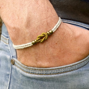 Peut inclure: Un bracelet tressé blanc et olive avec un accent de nœud doré.