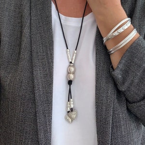 May include: A silver necklace with a leather cord and two heart charms. The necklace also features a silver bead with a textured surface.