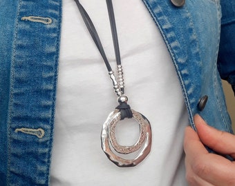 May include: A silver double circle pendant necklace with a black leather cord. The necklace is worn over a white t-shirt and a blue denim jacket.
