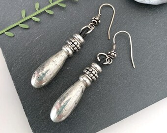 May include: A pair of silver dangle earrings with a teardrop-shaped pendant and a beaded detail.