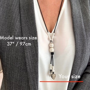 May include: A black leather necklace with silver beads and heart charms. The necklace is 37 inches long. Model wears size 37"/97cm.