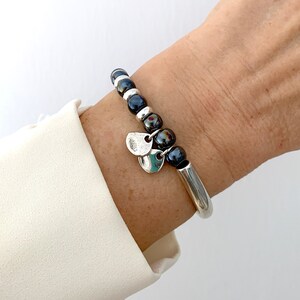 Pode incluir: Um bracelete de prata com contas pretas e pingentes de prata. O bracelete est&aacute; no pulso de uma pessoa.