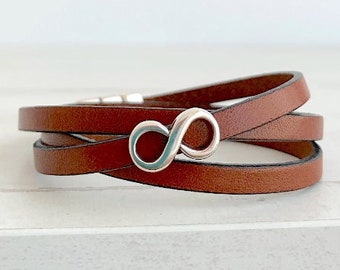 Op de afbeelding: Een bruin lederen armband met een zilveren oneindigheidssymbool bedel.