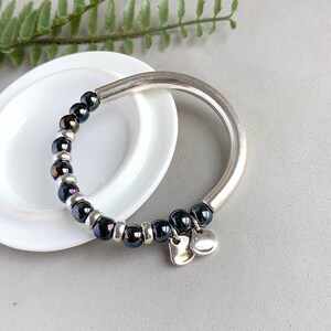 Pode incluir: Um bracelete de prata com contas pretas e dois pingentes de cora&ccedil;&atilde;o prateados.
