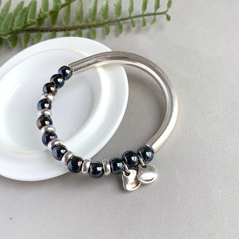 Pode incluir: Um bracelete de prata com contas pretas e dois pingentes de cora&ccedil;&atilde;o prateados.