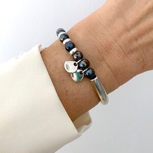 Pode incluir: Um bracelete de prata com uma fila de contas pretas e prateadas e dois pingentes de prata.
