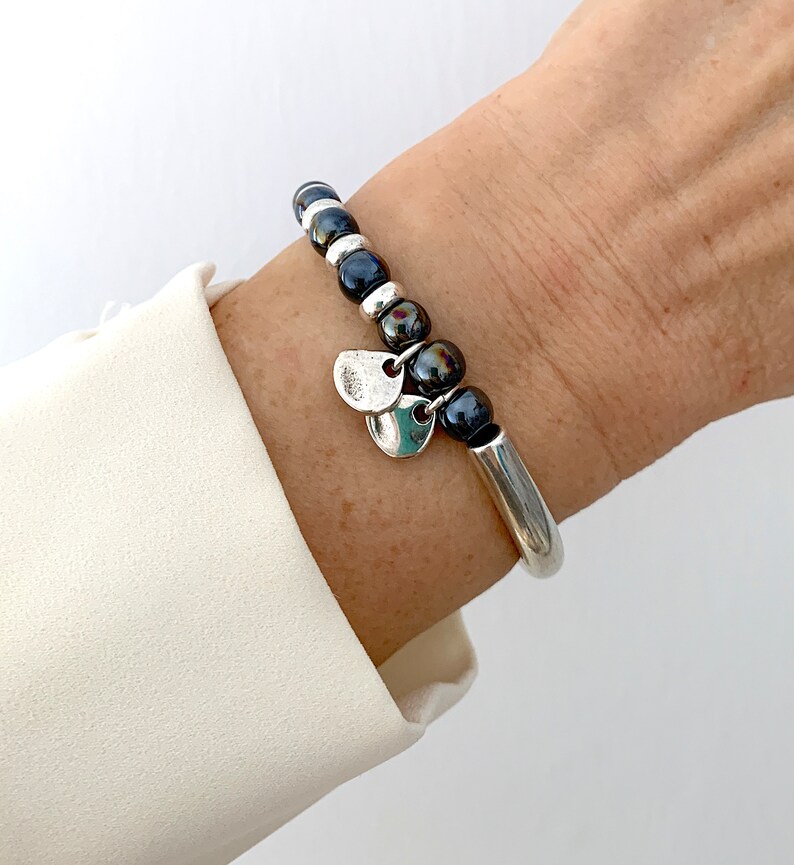 Pode incluir: Um bracelete de prata com uma fila de contas pretas e prateadas e dois pingentes de prata.