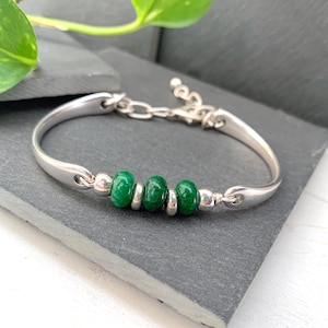 Può includere: Un braccialetto rigido in argento con chiusura a catena e quattro perle di pietre preziose verdi.
