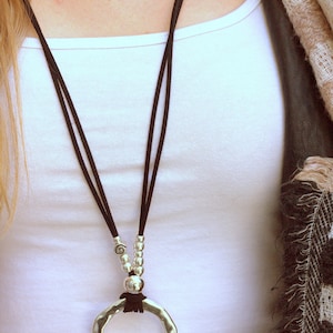May include: A silver pendant necklace with a large, round, hammered metal charm. The necklace is made with black cord and silver beads.