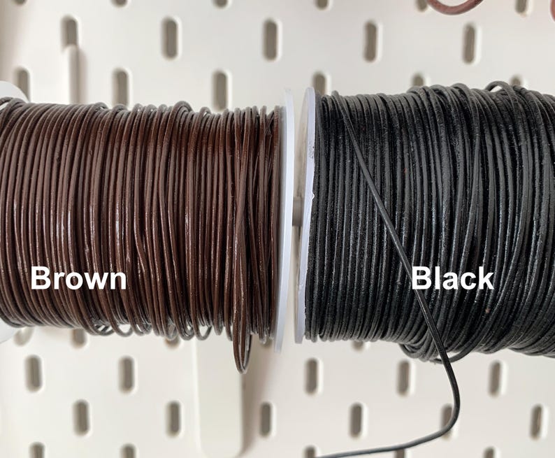 K&ouml;nnte beinhalten: Zwei Spulen Lederkordel, eine braune und eine schwarze, werden nebeneinander gezeigt. Die braune Kordel ist mit "Brown" und die schwarze Kordel mit "Black" beschriftet. Die Kordeln sind eng auf wei&szlig;en Spulen aufgewickelt.