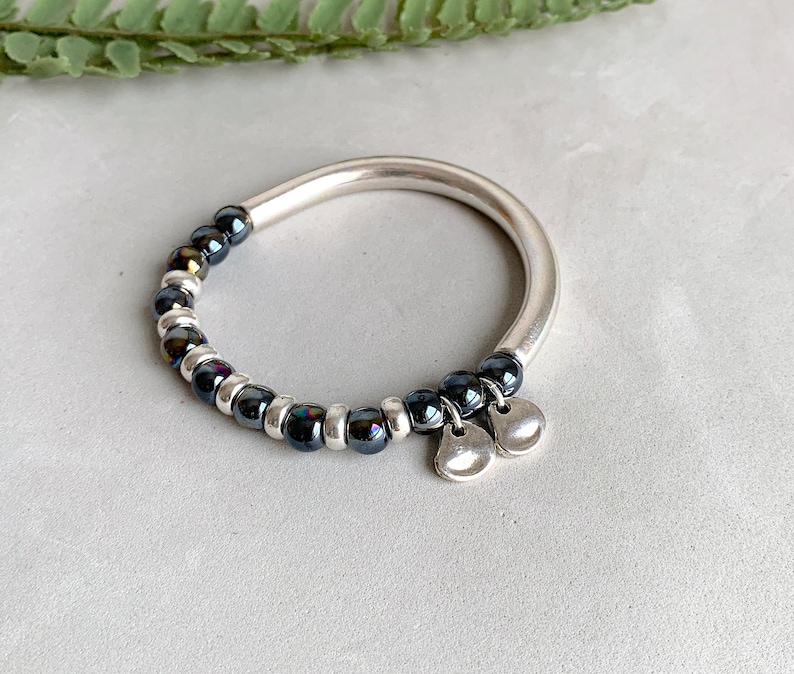 Pode incluir: Um bracelete de prata com contas pretas iridescentes e dois pingentes de prata.