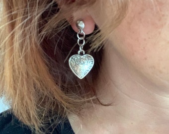 May include: Silver heart-shaped dangle earrings with a chain and a small bead at the top.