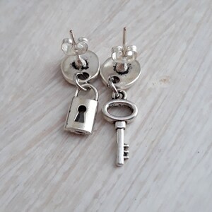 May include: A pair of silver earrings with a lock and key charm. The lock is on the left earring and the key is on the right earring.