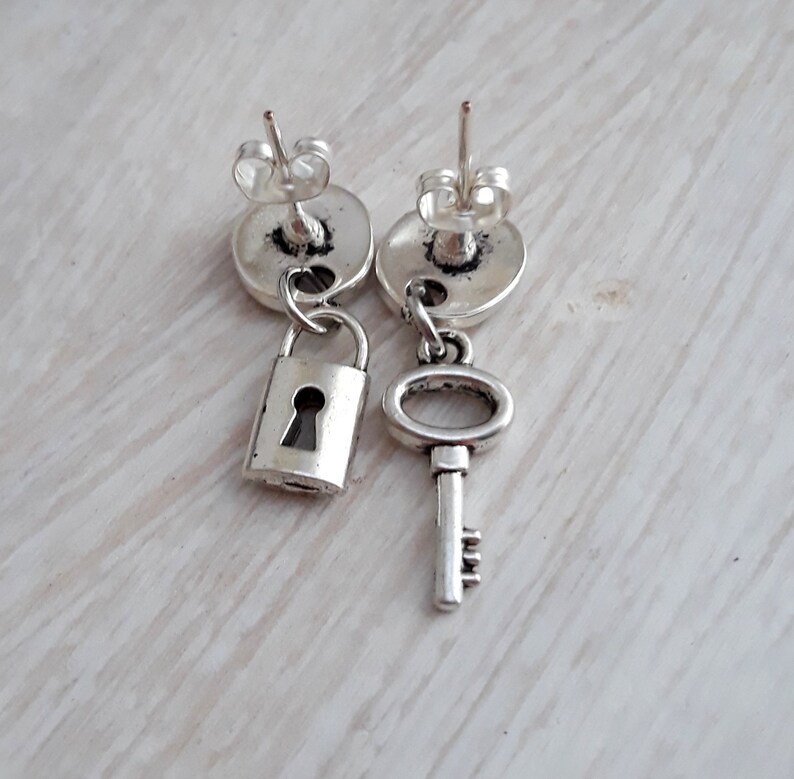 May include: A pair of silver earrings with a lock and key charm. The lock is on the left earring and the key is on the right earring.