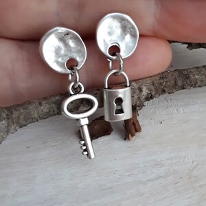 May include: A pair of silver earrings with a key and a padlock charm. The earrings are made of hammered metal and have a simple design.