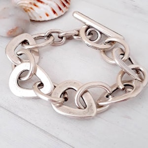 Puede incluir: Un brazalete de cadena gruesa de plata con cierre de palanca. El brazalete está hecho de eslabones grandes de forma ovalada.
