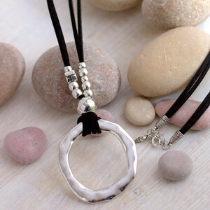 May include: A silver pendant necklace with a large, hammered, circular pendant. The necklace has a black suede cord and silver beads.