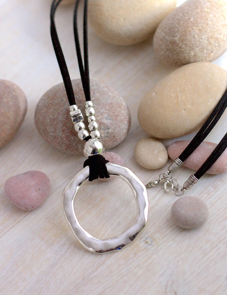 May include: A silver pendant necklace with a large, hammered, circular pendant. The necklace has a black suede cord and silver beads.