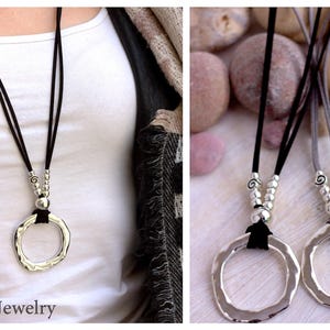 May include: Two silver pendant necklaces with a hammered circle design. The necklaces are on black and gray suede cords with silver bead accents. The necklaces are displayed on a white surface with gray stones.