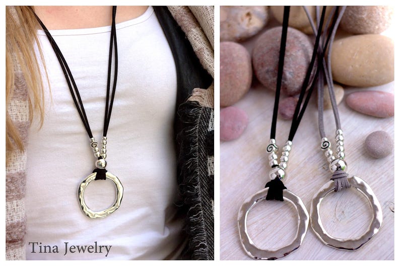 May include: Two silver pendant necklaces with a hammered circle design. The necklaces are on black and gray suede cords with silver bead accents. The necklaces are displayed on a white surface with gray stones.