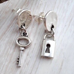 May include: A pair of silver earrings with a key and a padlock charm. The earrings are made of metal and have a simple design.
