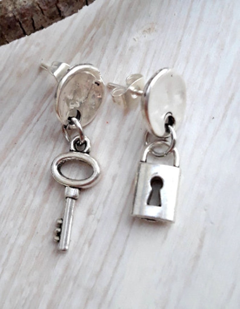 May include: A pair of silver earrings with a key and a padlock charm. The earrings are made of metal and have a simple design.