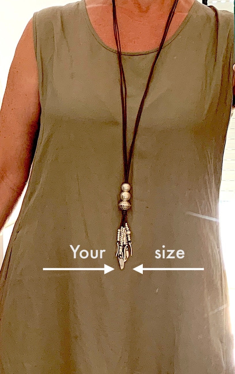 K&ouml;nnte beinhalten: Eine lange braune Halskette mit silberfarbenen Perlen und einem dekorativen Anh&auml;nger h&auml;ngt &uuml;ber einem &auml;rmellosen olivgr&uuml;nen Kleid. Der Text "Your size" ist mit Pfeilen auf dem Bild geschrieben, die auf die Halskette zeigen.