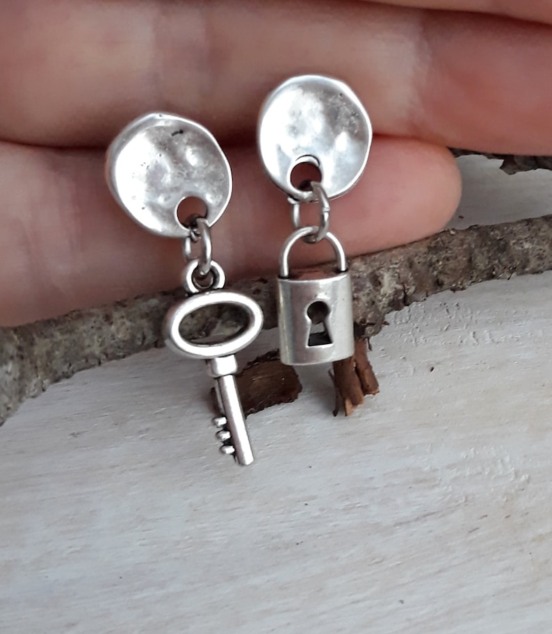 May include: A pair of silver earrings with a key and a padlock charm. The earrings are made of hammered metal and have a simple design.