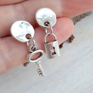 May include: A pair of silver earrings, one with a key charm and the other with a padlock charm. Both charms are attached to a hammered silver disc.