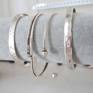 Op de afbeelding: Vier zilveren armbanden, twee met een getextureerd oppervlak en twee met een glad oppervlak. Een armband heeft een kleine bal aan het einde.