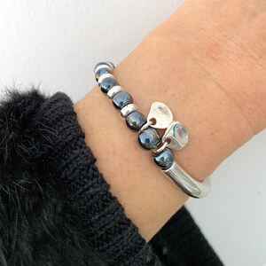 Pode incluir: Um bracelete de prata com uma fila de contas pretas e um fecho de cora&ccedil;&atilde;o de prata.