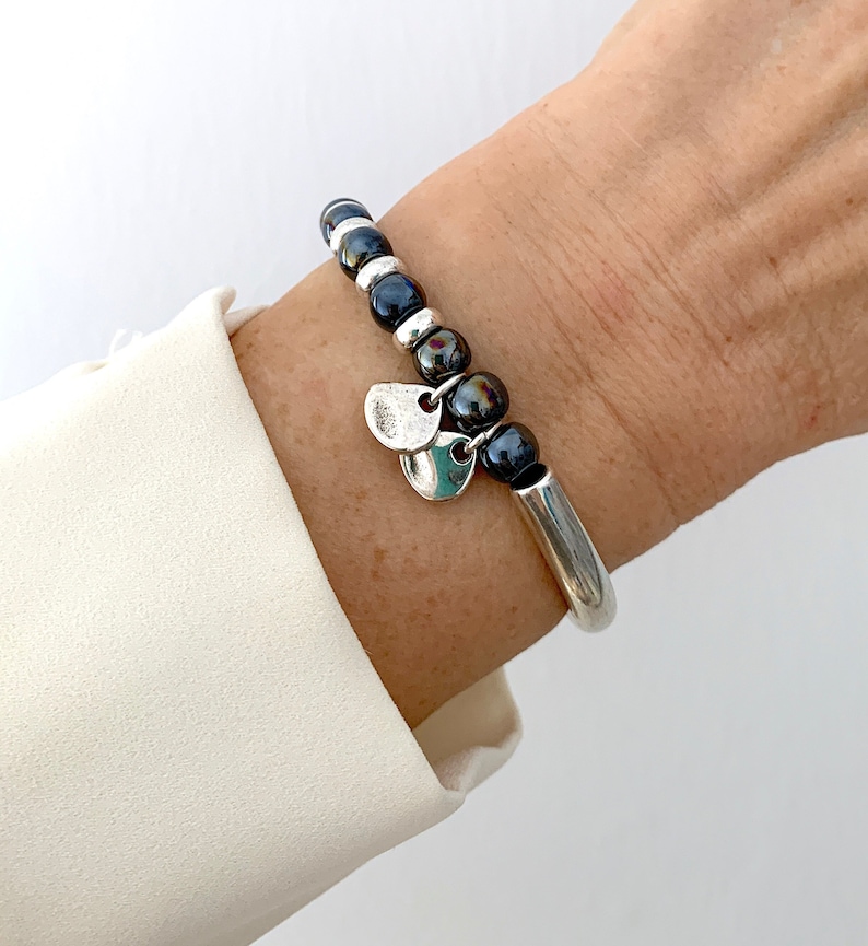 Pode incluir: Um bracelete de prata com contas pretas e pingentes de prata. O bracelete est&aacute; no pulso de uma pessoa.