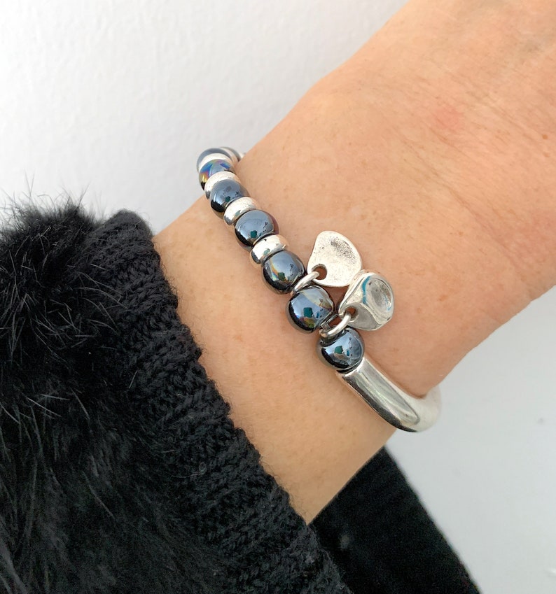 Pode incluir: Um bracelete de prata com uma fila de contas pretas e um fecho de cora&ccedil;&atilde;o de prata.