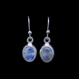 May include: A pair of silver drop earrings featuring oval-shaped moonstones with a blue iridescent sheen. Each stone is set in a smooth silver bezel, suspended from a simple silver hook wire, showcasing a polished metallic finish.