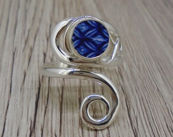 May include: A silver ring with a blue and white patterned ceramic inlay. The ring is designed with a twisted band and a single, round stone.
