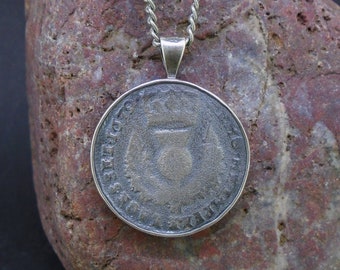 May include: A circular pendant necklace featuring a dark, weathered coin with a central thistle emblem, encased in a simple silver-toned metal bezel and suspended from a matching silver-toned twisted metal chain link necklace.