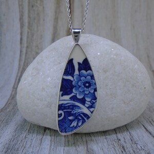 May include: A blue and white porcelain pendant necklace with a floral design. The pendant is shaped like a teardrop and is set in a silver frame.