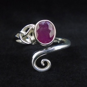May include: A silver ring featuring a pink gemstone set in a Celtic knot design. The ring has a swirling band.