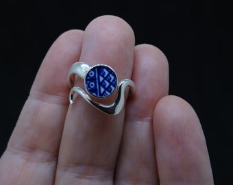 May include: A silver ring with a blue and white patterned ceramic inlay. The ring has a wavy design.