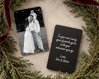 May include: Two rectangular metal wallet cards. One card features a black and white photograph of an adult holding a child. The other black card displays white text: So you can carry your favorite girls with you wherever you go. Love, Em & Chloe.