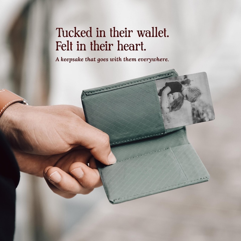 May include: A sage green wallet featuring a diagonal textured pattern and a rectangular metal insert displaying a black and white photograph of two children. The text reads: Tucked in their wallet. Felt in their heart. A keepsake that goes with them everywhere.