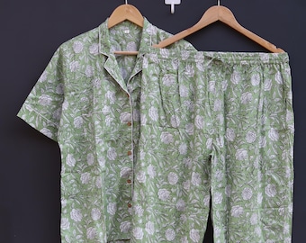May include: A sage green pajama set featuring a white floral pattern, including a short-sleeved button-down shirt with a collar and matching pants with an elastic waistband. The fabric displays the text Babita Tex in a white script font.