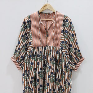 以下が含まれることがあります： 白と茶色のストライプのドレスに花柄がプリントされています。ドレスはVネックで、袖は3/4袖です。