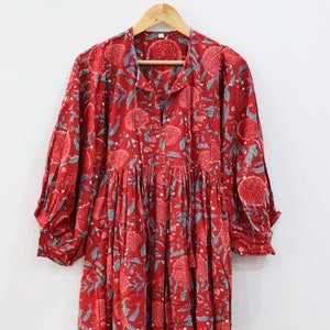 Könnte beinhalten: Ein rotes Baumwollkleid mit Blumenmuster. Das Kleid hat einen V-Ausschnitt, 3/4 Ärmel und einen gerafften Rock.