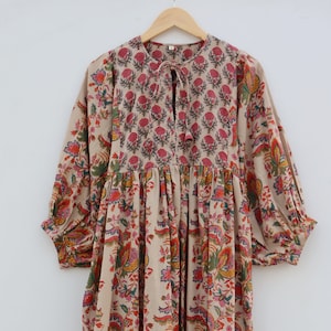 May include: A beige maxi dress with a floral print. The dress has a tie at the neckline and a tiered skirt. The skirt is a mix of red, blue, and beige stripes.