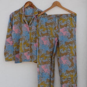 May include: A gray pajama set with a long-sleeved shirt and pants. The fabric features a repeating pattern of pink, yellow, and brown leopards.