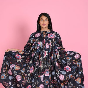 Op de afbeelding: Een zwarte maxi-jurk met een bloemenprint. De jurk heeft een geplooide buste en een zwierige rok. Het model draagt de jurk met bruine sandalen.