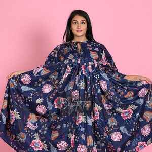 Peut inclure: Une robe maxi bleu marine à imprimé floral. La robe a une taille froncée et un nœud au niveau de l'encolure. Le mannequin porte la robe avec des sandales brunes.